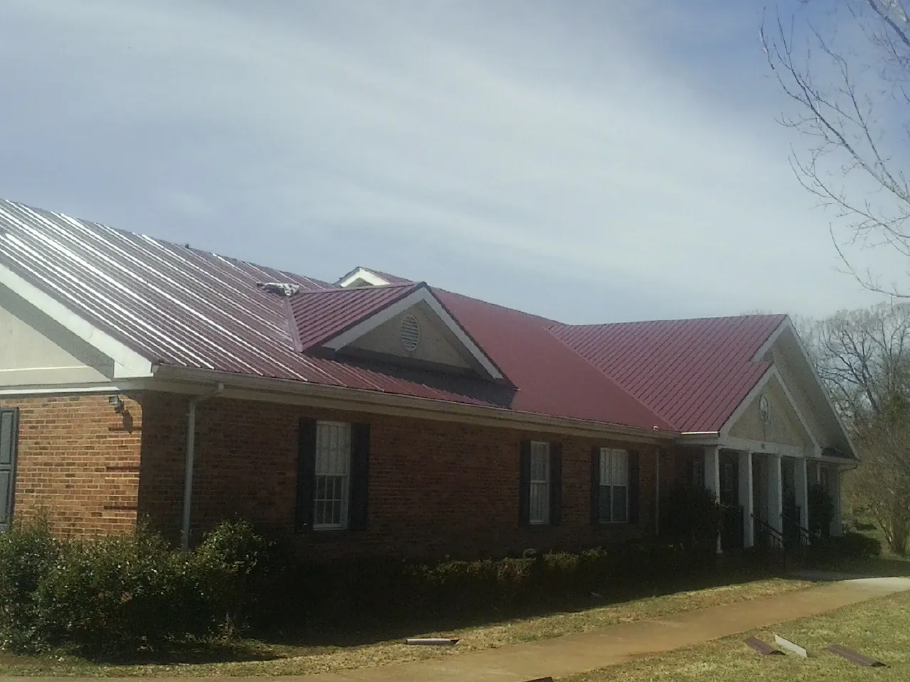 Red metal roof with gabled entries on a long brick building, from a Hail Damage Roof Repair job in Palos Heights