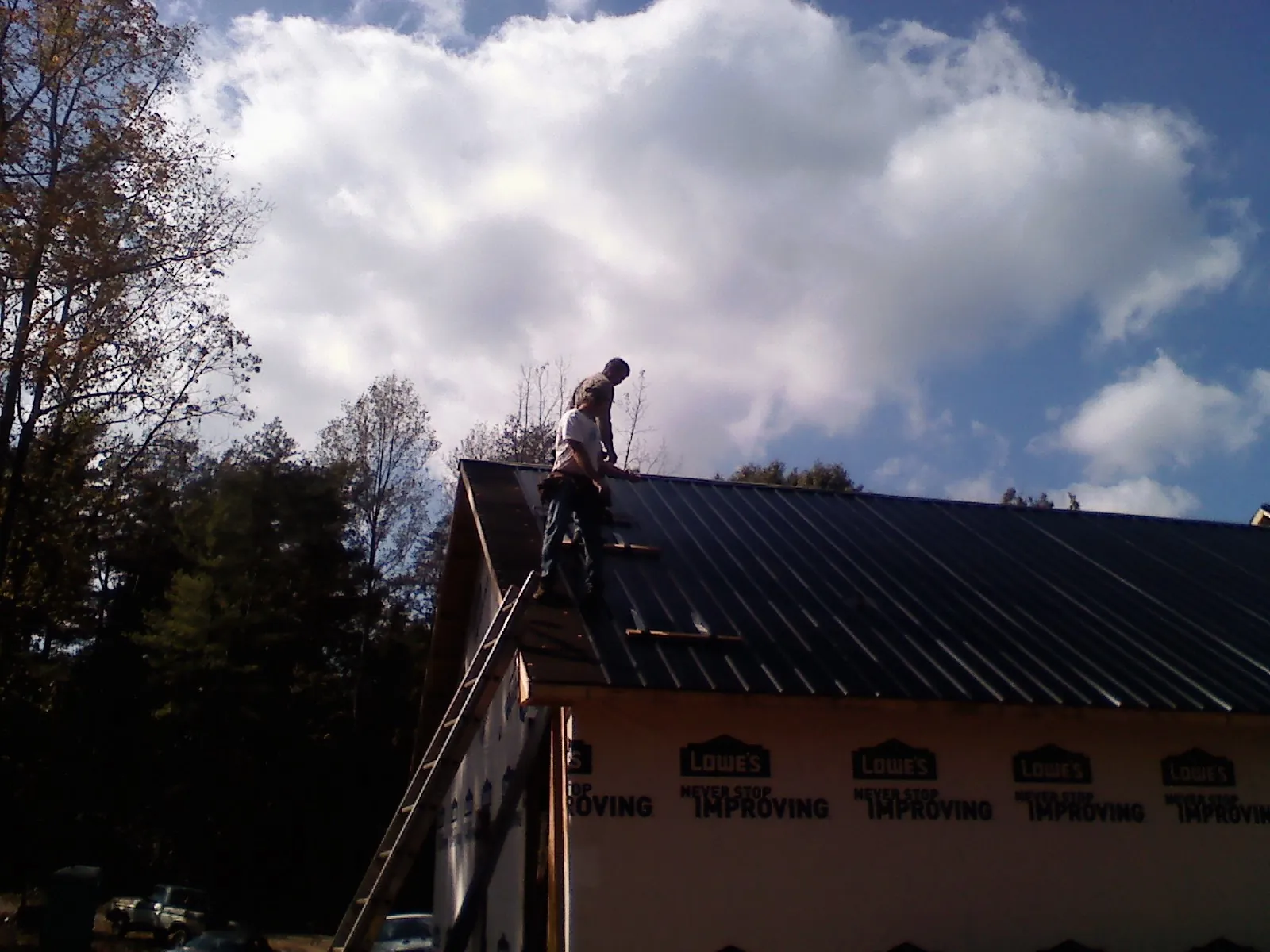 Roofer fastening dark metal panels high against a cloudy sky, from a Roof Inspection job in Palos Heights