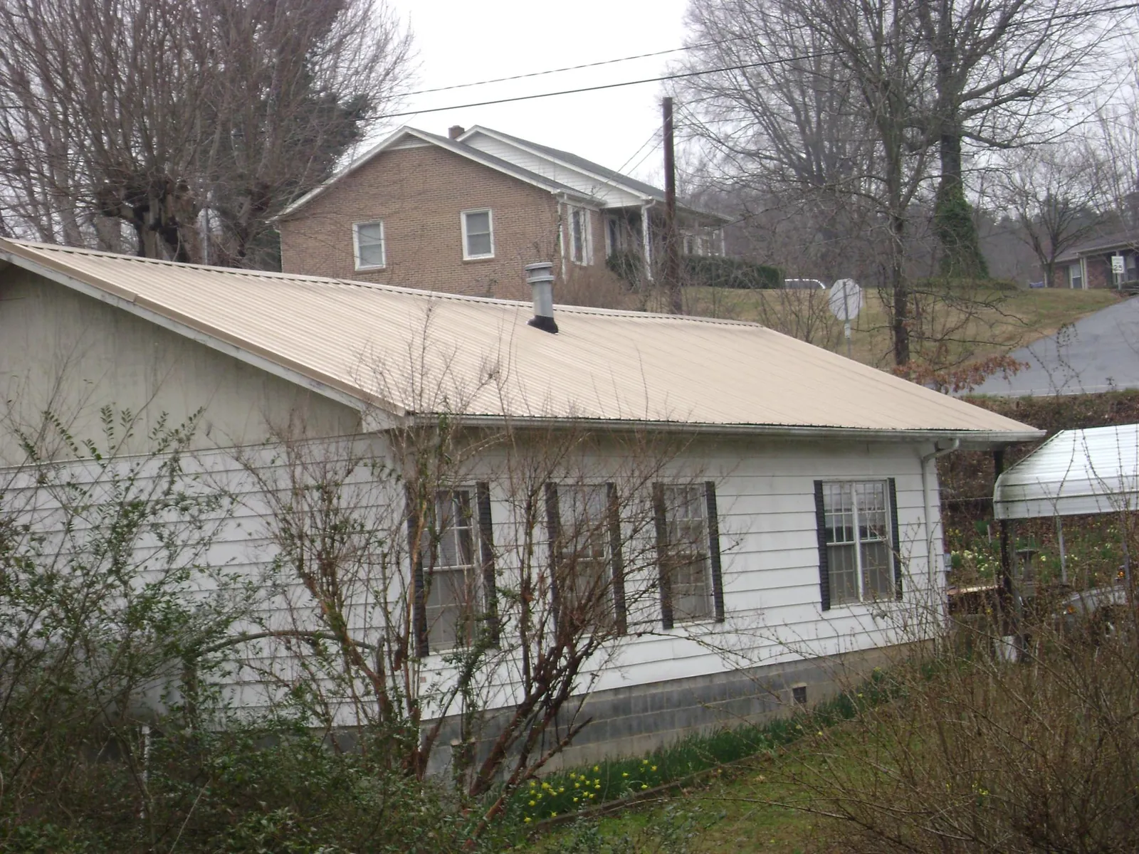 Tan metal roof on a white sided house set into a hillside — Commercial Roofing by Roofing Brothers in Palos Heights